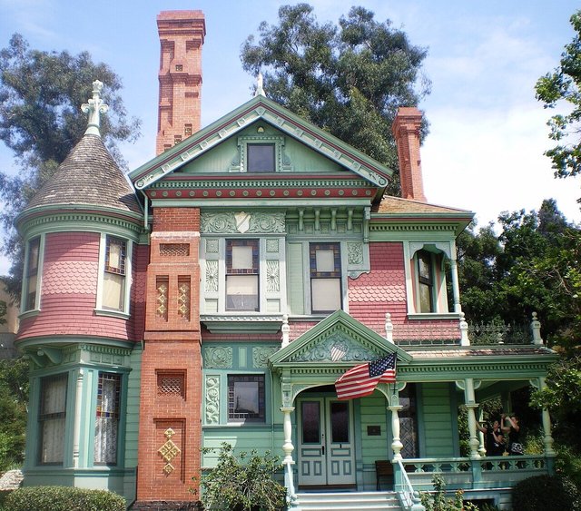 Victorian house with brick chimneys, a turret and a green and pink painted porch at Heritage Square Museum