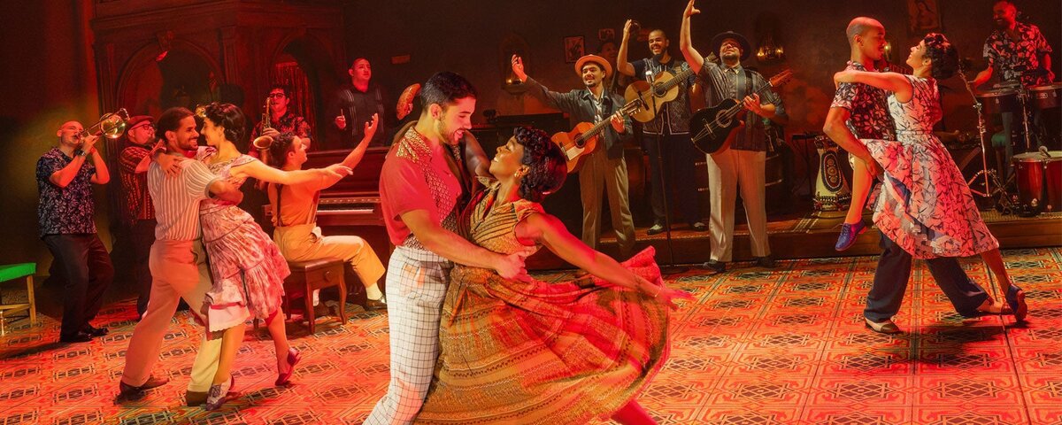 Dancing couples in a warmly lit Havana club set with a live band of horns and guitars behind them