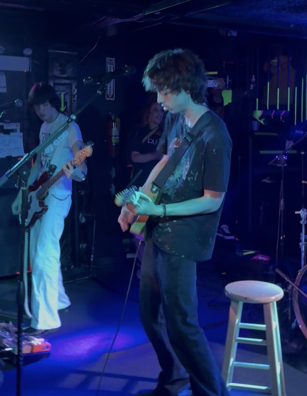 Two guitarists performing on a dim, blue-lit club stage