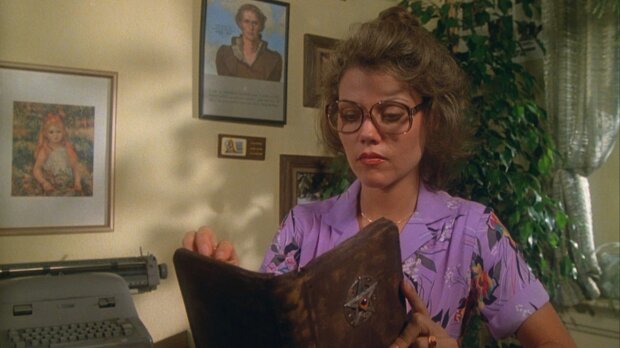 Woman in glasses and a purple floral blouse reading an old leather book in a film still