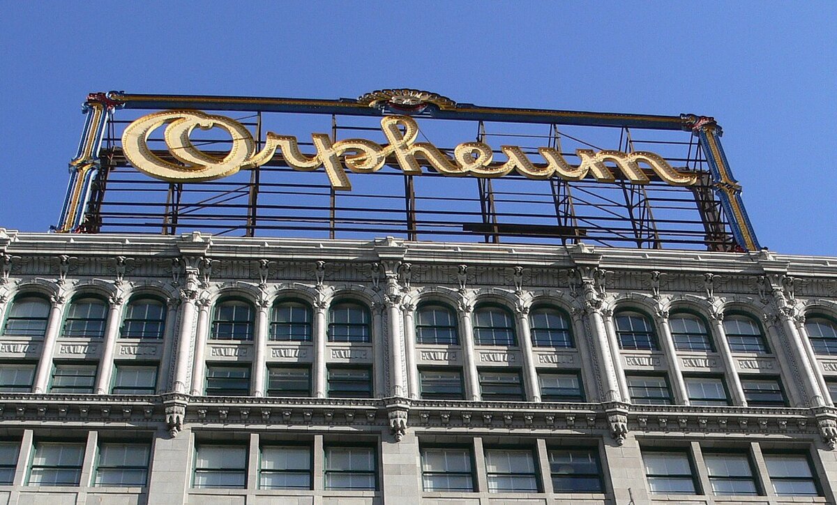 Gold Orpheum rooftop sign above the ornate upper facade of the theatre building against a blue sky