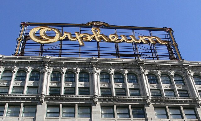 Gold Orpheum rooftop sign above the ornate upper facade of the theatre building against a blue sky