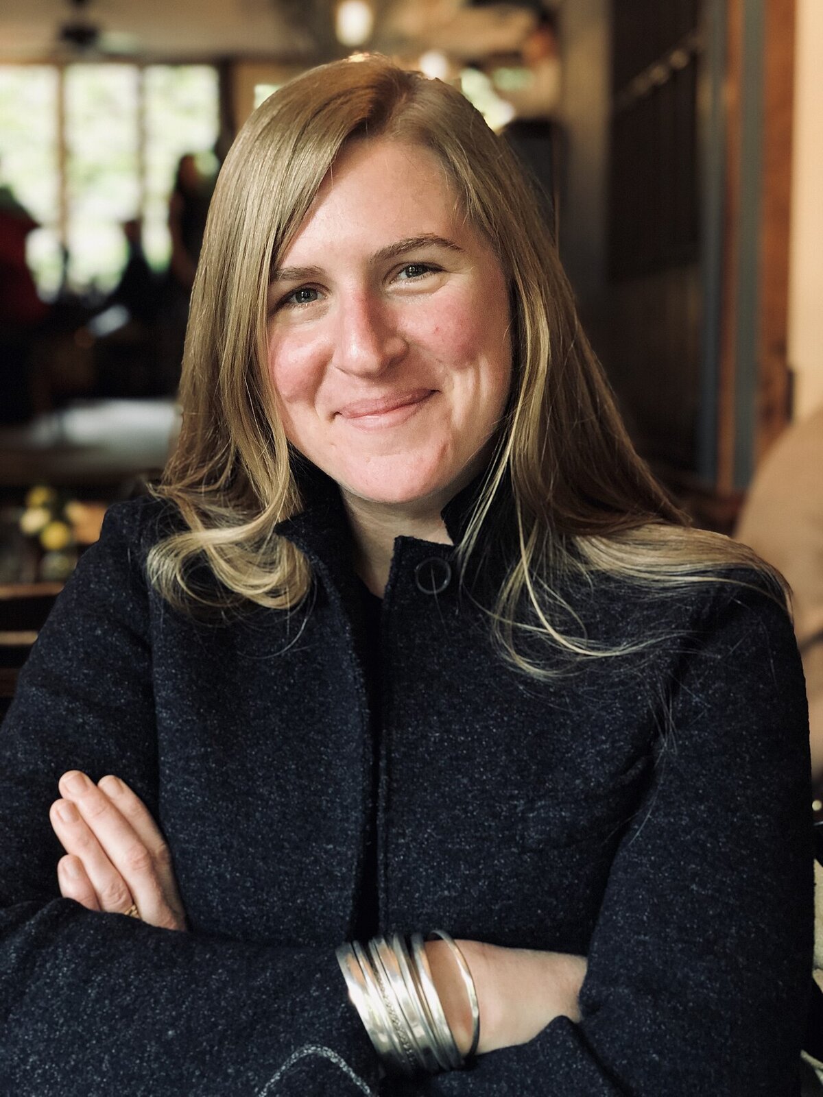 Portrait of Phoebe Judge smiling with arms crossed, wearing a dark wool coat