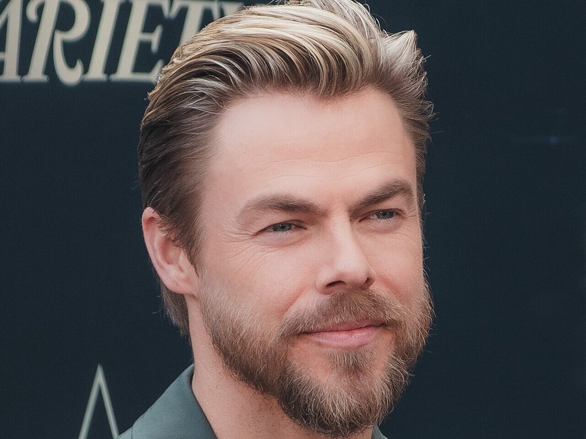 Derek Hough smiling in a sage green jacket at a Hollywood Walk of Fame ceremony