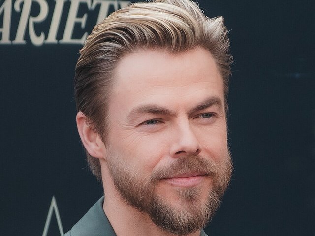 Derek Hough smiling in a sage green jacket at a Hollywood Walk of Fame ceremony