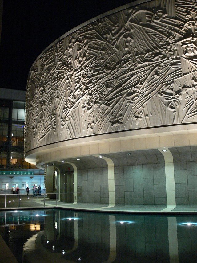 Night view of the Mark Taper Forum's curved, sculpted exterior wall above a reflecting pool at the Music Center