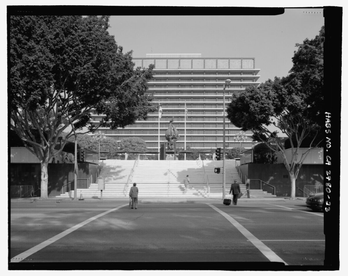 Black-and-white view across Grand Avenue to the broad stairs of the Los Angeles Music Center, with a tall office tower behind