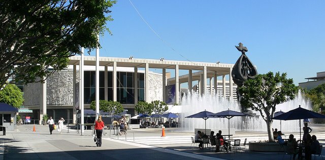 Sunlit Music Center plaza on Grand Avenue with a fountain, a bronze sculpture and visitors at outdoor tables