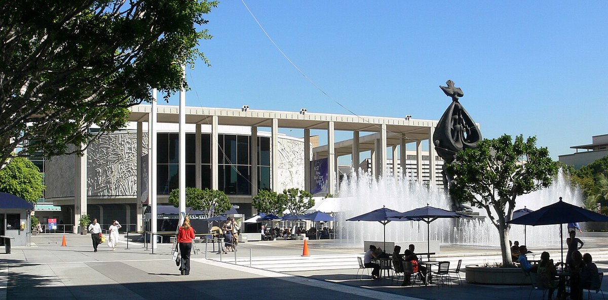 Sunlit Music Center plaza on Grand Avenue with a fountain, a bronze sculpture and visitors at outdoor tables
