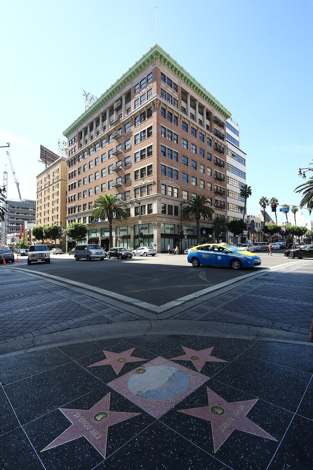 Street corner in Hollywood with a brick high-rise, a taxi and Walk of Fame stars on the sidewalk