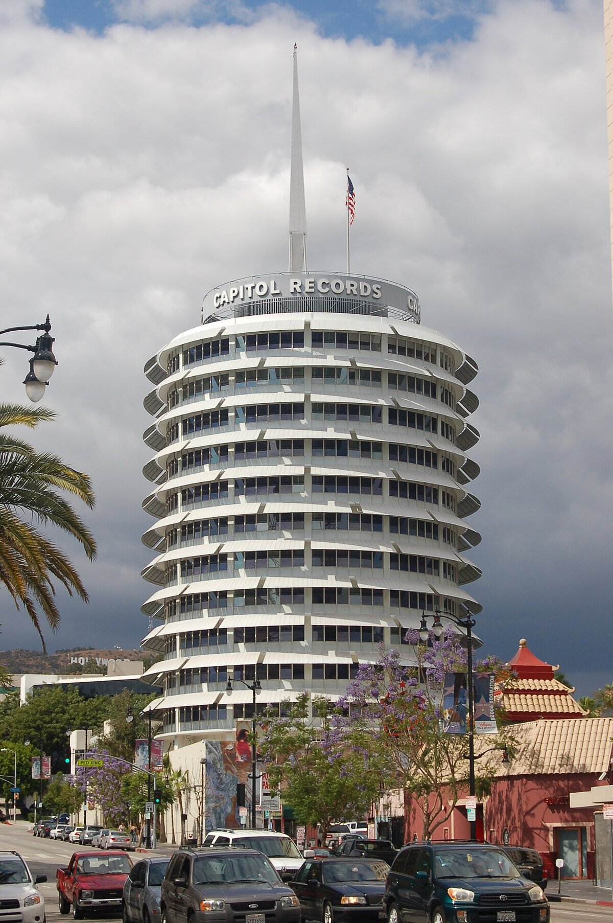 The round Capitol Records tower on Vine Street in Hollywood under a cloudy sky, with palm trees and traffic below