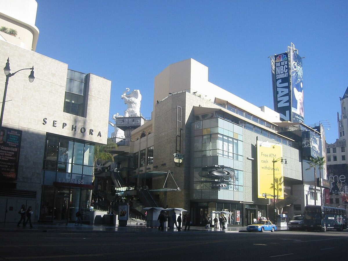Hollywood and Highland shopping complex on a sunny day, with a taxi and pedestrians along Hollywood Boulevard.