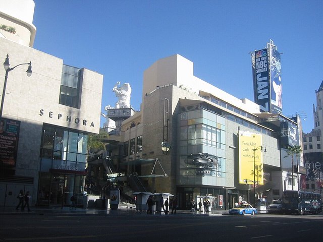 Hollywood and Highland shopping complex on a sunny day, with a taxi and pedestrians along Hollywood Boulevard.