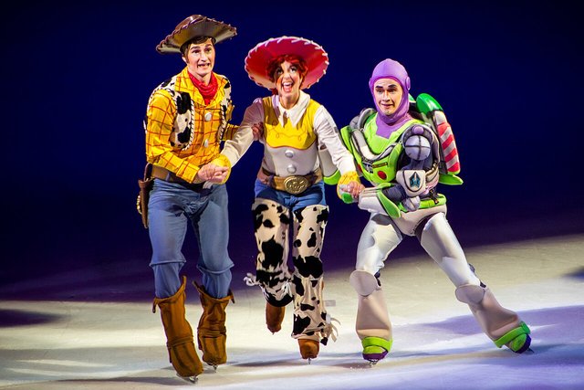 Skaters dressed as Woody, Jessie and Buzz Lightyear glide hand in hand across a spotlit Disney On Ice rink