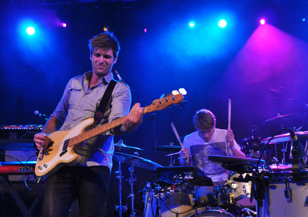 Bassist and drummer performing on stage under blue and magenta lights