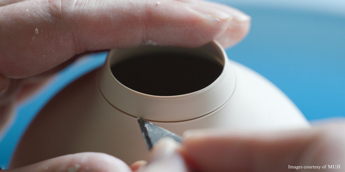 Close-up of hands shaping the rim of a pale ceramic vessel with a small tool