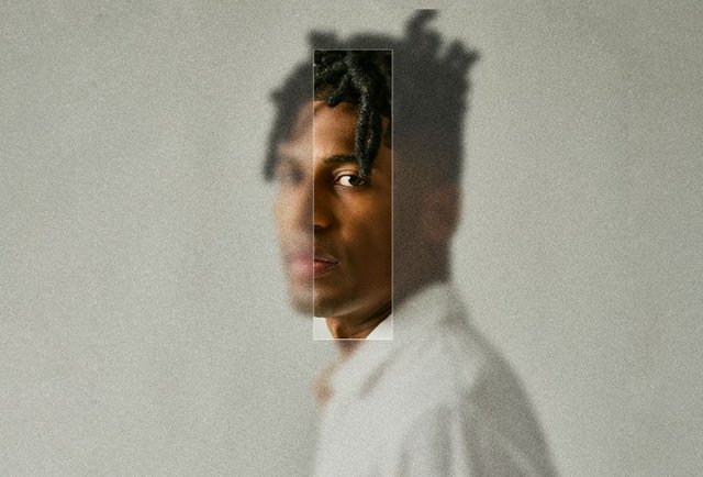 Portrait of Jon Batiste in a white shirt against a gray backdrop