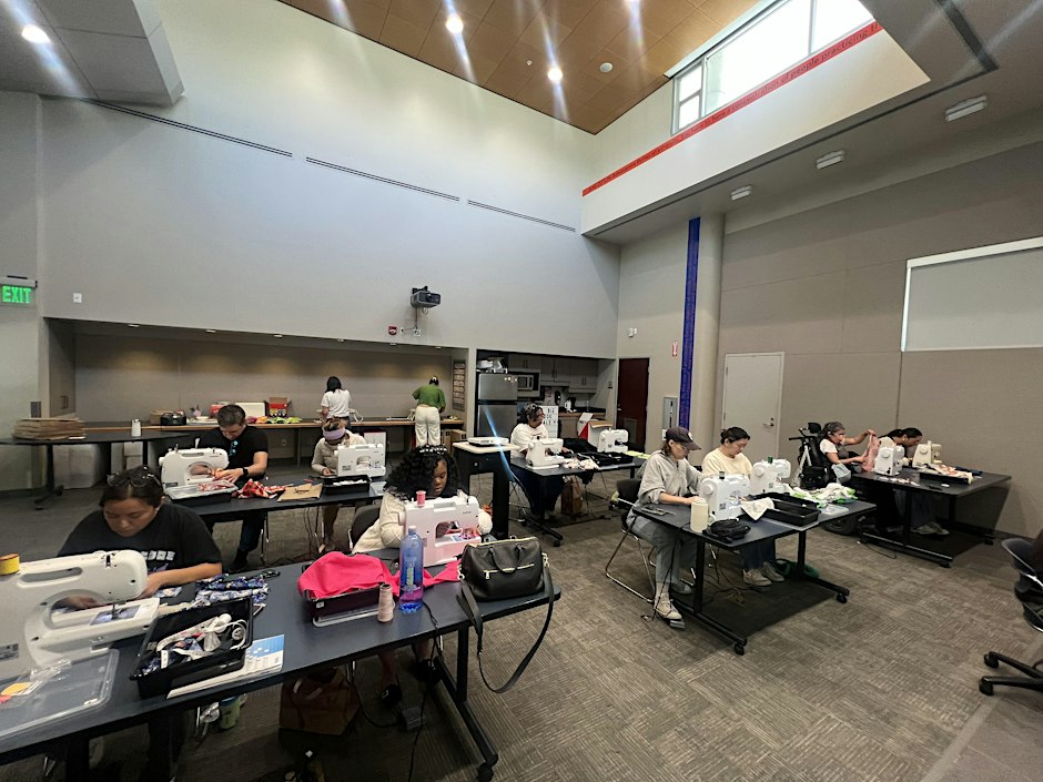 Workshop attendees sewing at machines on long tables in a library community room