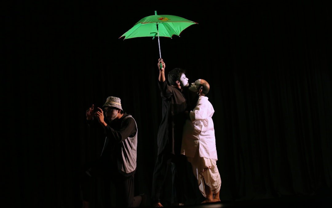 A theater performer holding a green umbrella on stage in dramatic lighting