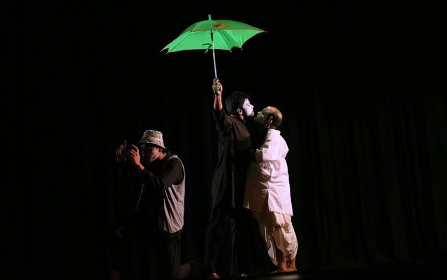 A theater performer holding a green umbrella on stage in dramatic lighting
