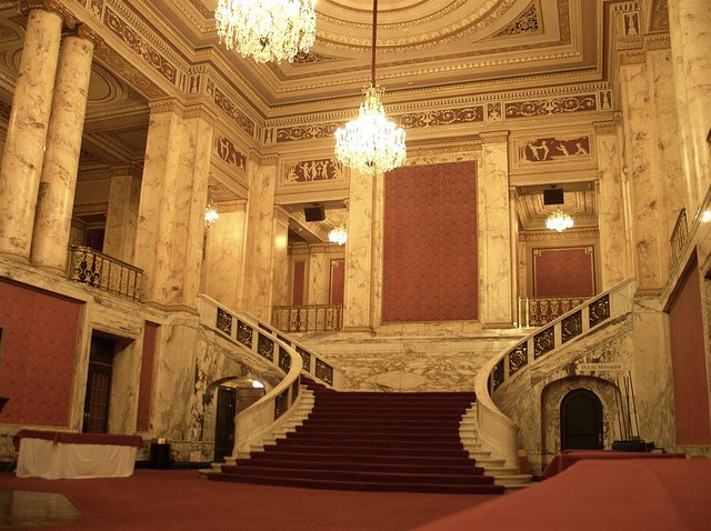 A marble staircase and chandeliers in the grand lobby of a historic theatre