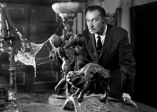 Black-and-white film still of Vincent Price leaning over a cobweb-covered table with a statue and a sculpted panther