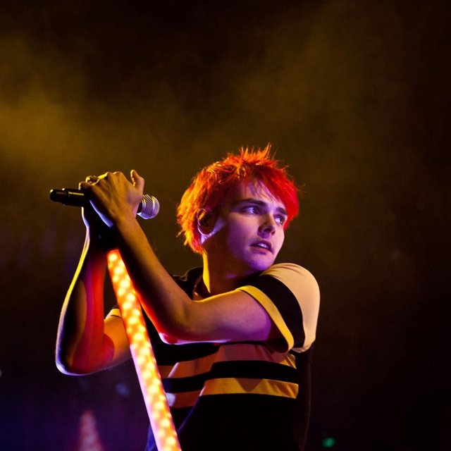 Singer with bright red hair gripping a microphone stand lit with warm stage lights in a haze of smoke