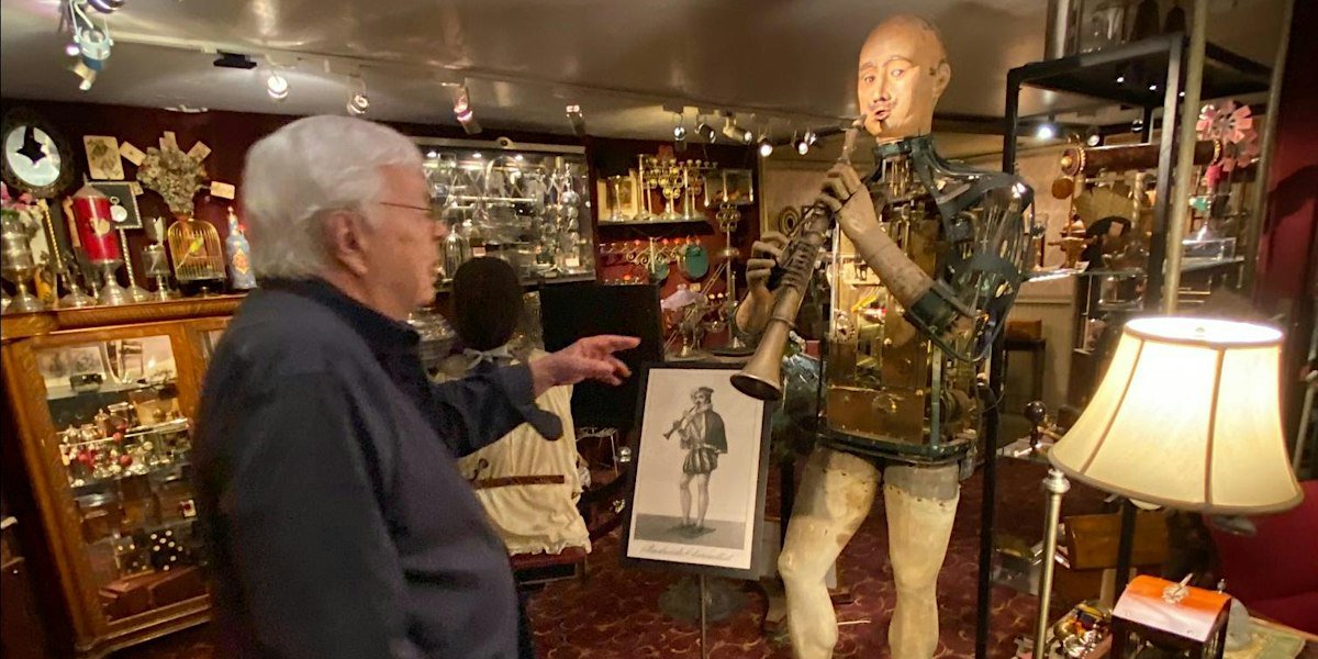 A row of antique clockwork automaton figures displayed in a collector's workshop