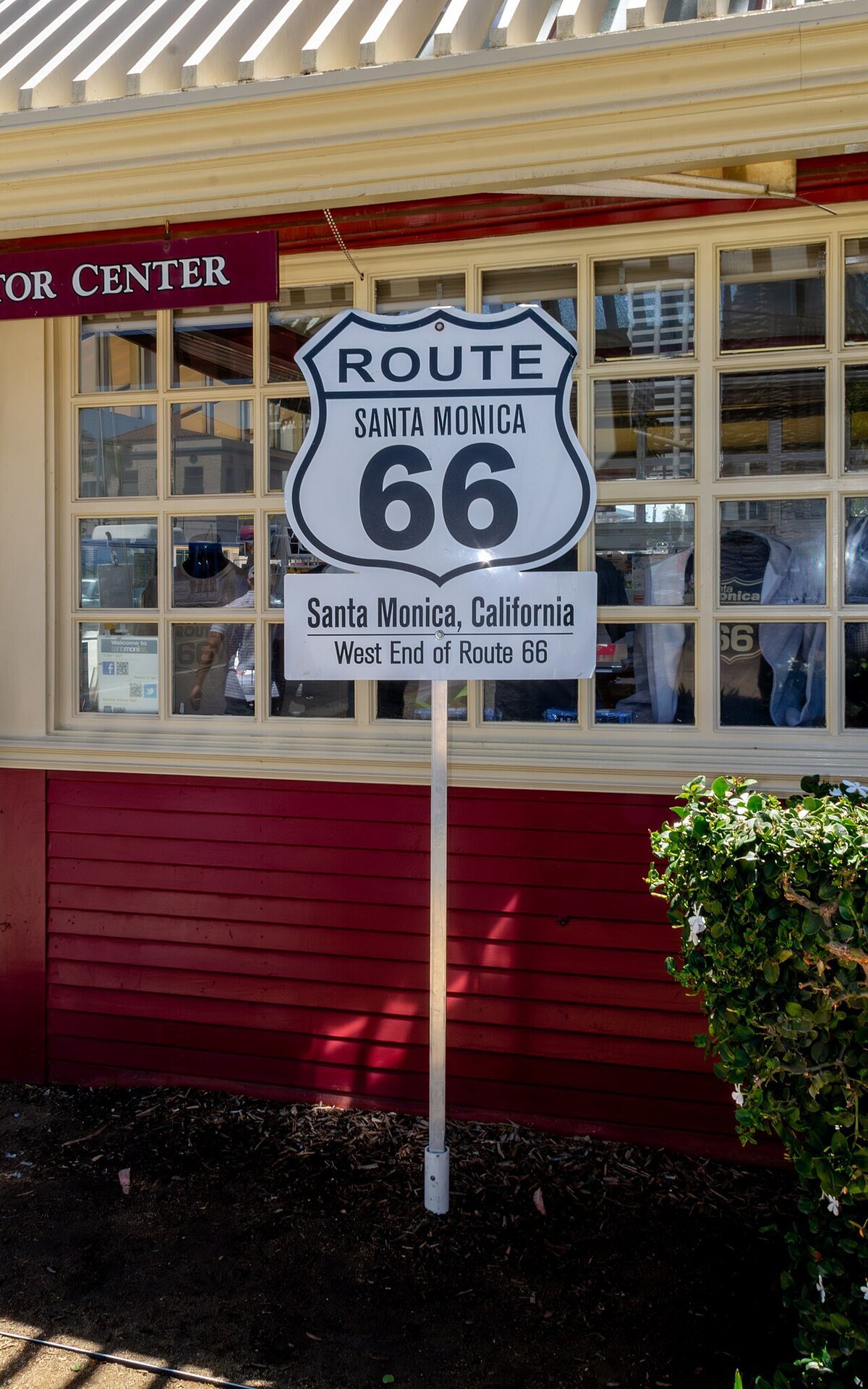 White Route 66 shield sign reading Santa Monica, California, West End of Route 66, mounted outside a red and cream building