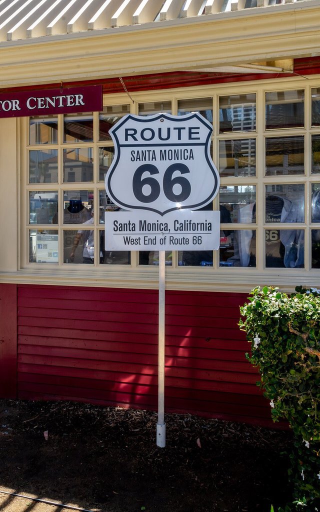 White Route 66 shield sign reading Santa Monica, California, West End of Route 66, mounted outside a red and cream building