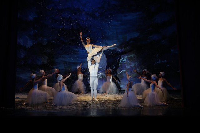 Ballerina lifted high above a stage of dancers in white tutus under a snowy blue backdrop