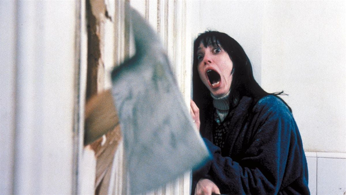 Film still of a woman in a blue robe screaming as an axe splinters a bathroom door
