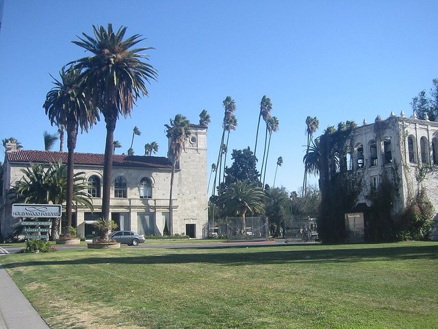 Hollywood Forever's stone administration building and tall palm trees beside a green lawn under a blue sky