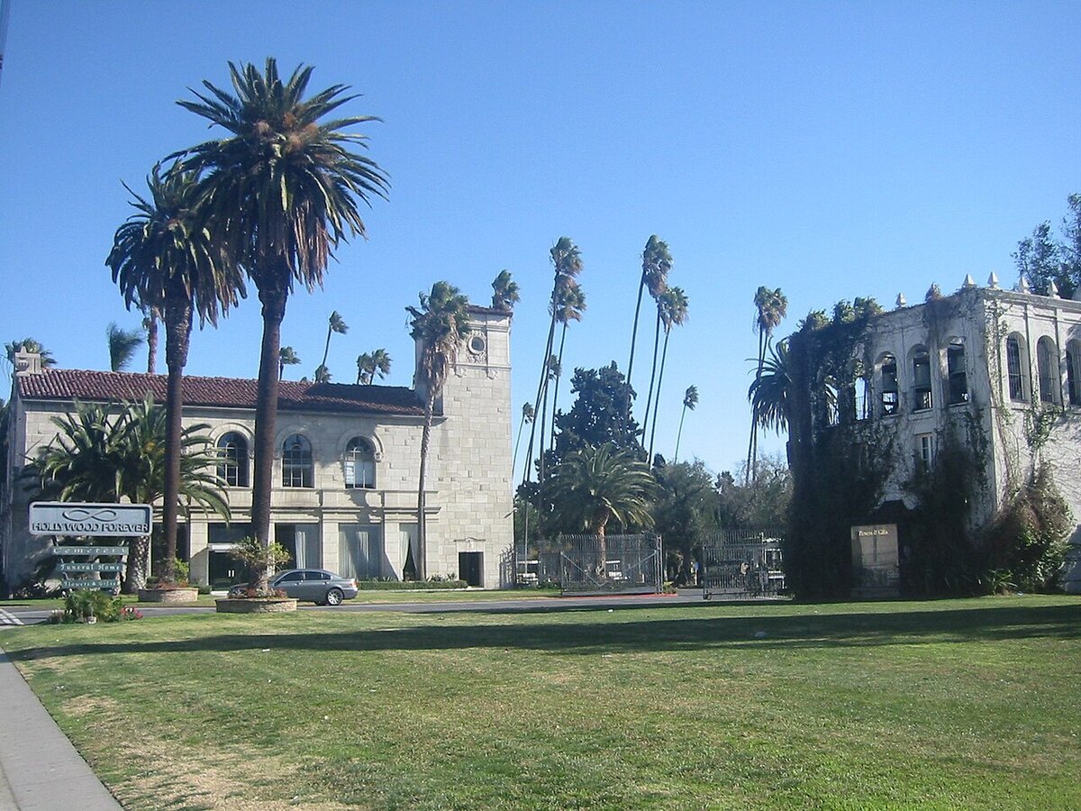 Hollywood Forever's stone administration building and tall palm trees beside a green lawn under a blue sky