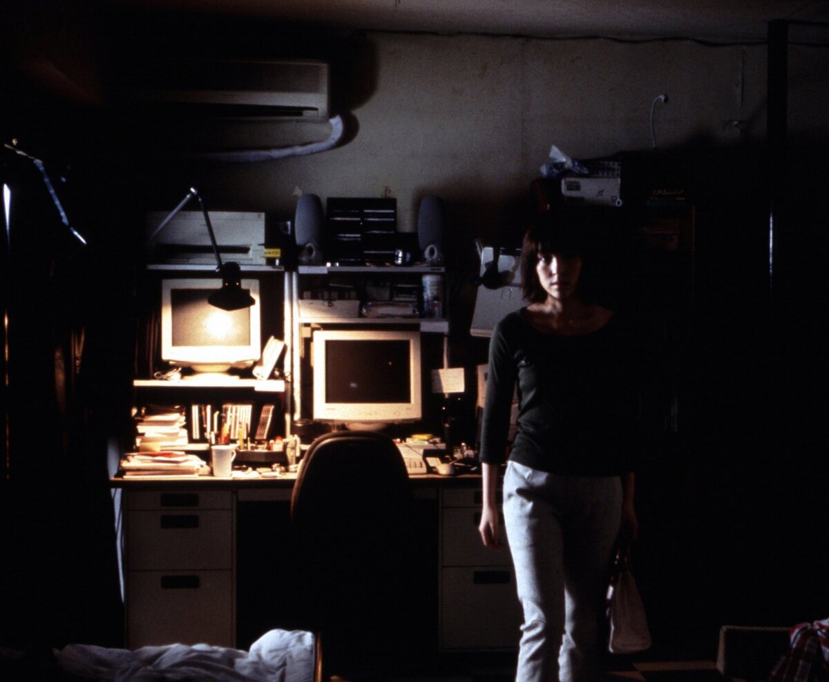 Dark apartment with glowing computer monitors and a woman standing in the shadows, a still from the film Pulse