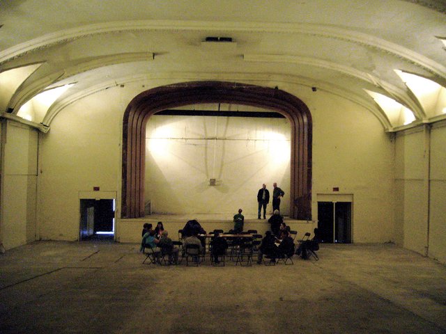The Regent Theater's arched proscenium stage on Main Street, with a small group seated on the floor below it