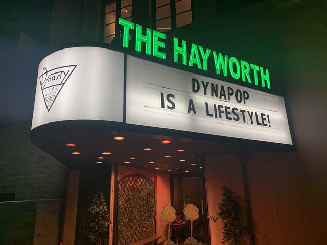 Night exterior of Dynasty Typewriter at The Hayworth, with green neon marquee and lit entryway