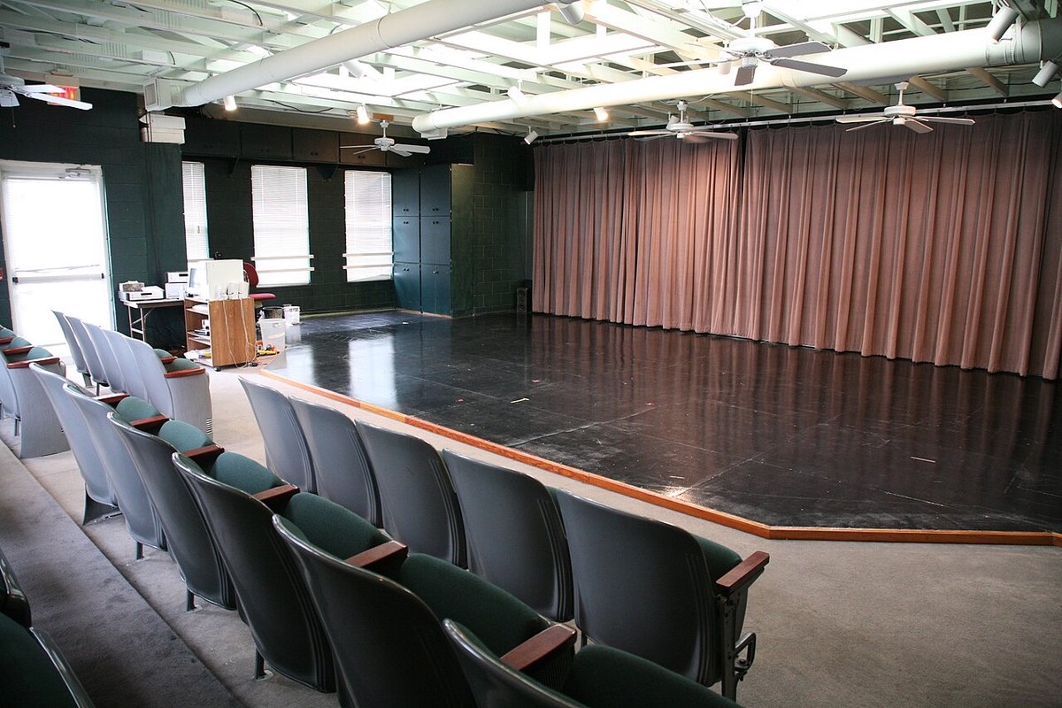 A small black-box studio theatre with a bare stage, curtain and tiered seating