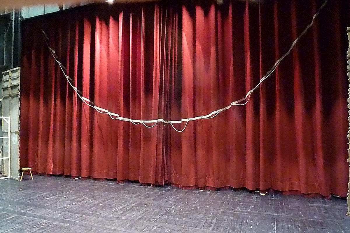 A red theatre curtain hanging across a stage with a white rope looped along it