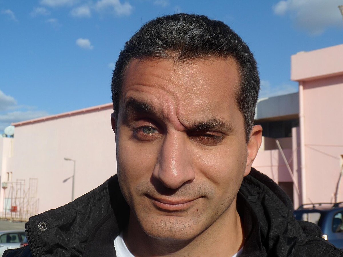 Bassem Youssef speaking at a public event, wearing a dark suit