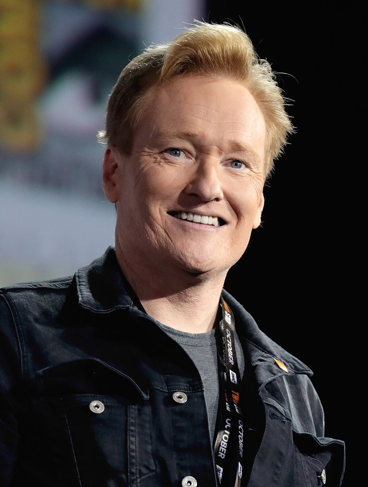 Smiling Conan O'Brien in a dark denim jacket at a convention panel