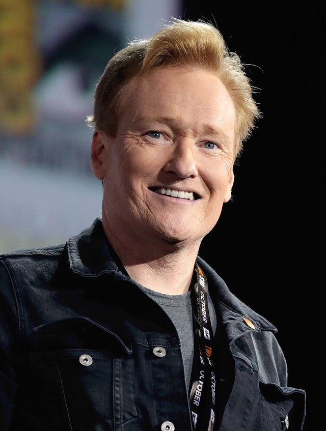 Smiling Conan O'Brien in a dark denim jacket at a convention panel