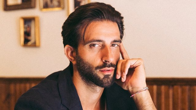 Davide De Pierro, dark-haired and bearded, resting his chin on his hand in a wood-paneled room