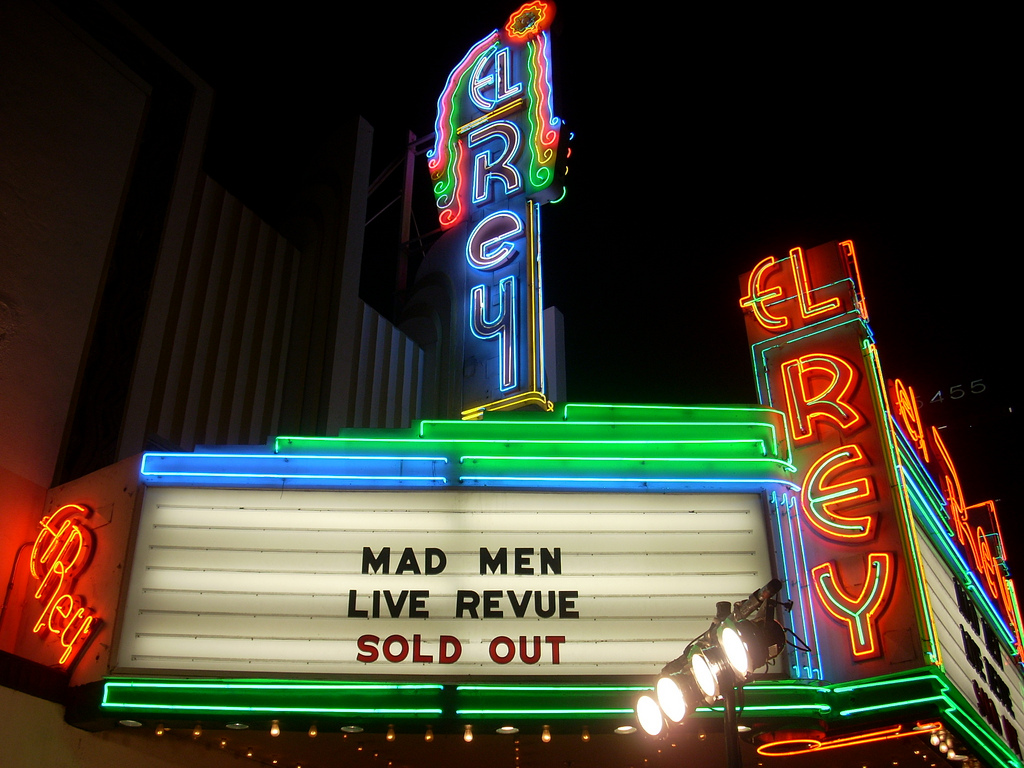 The El Rey Theatre's neon vertical sign and lit marquee glowing on Wilshire Blvd. at night
