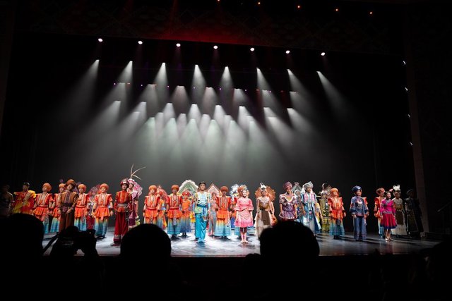 Performers in colorful costumes taking a bow on a live stage in front of an audience