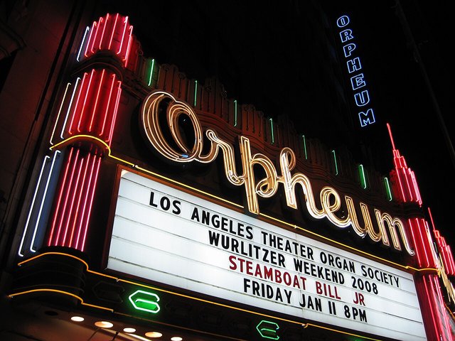 The Orpheum Theatre's neon script sign and lit marquee glowing red, green and gold at night above Broadway in Downtown Los Angeles