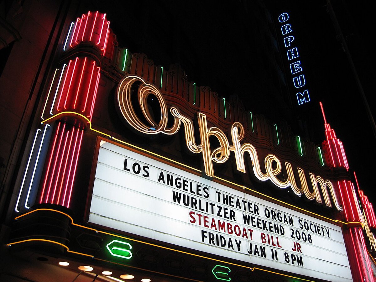 The Orpheum Theatre's neon script sign and lit marquee glowing red, green and gold at night above Broadway in Downtown Los Angeles
