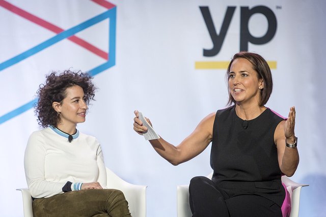 Ilana Glazer, with curly dark hair and a white sweater, seated onstage during a panel conversation