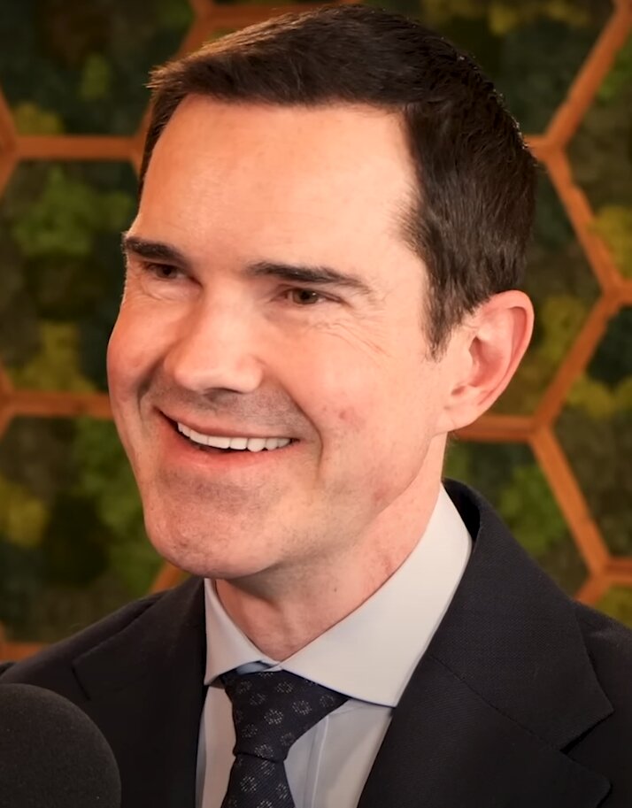 Close-up portrait of a smiling man in a dark suit and tie speaking into a microphone