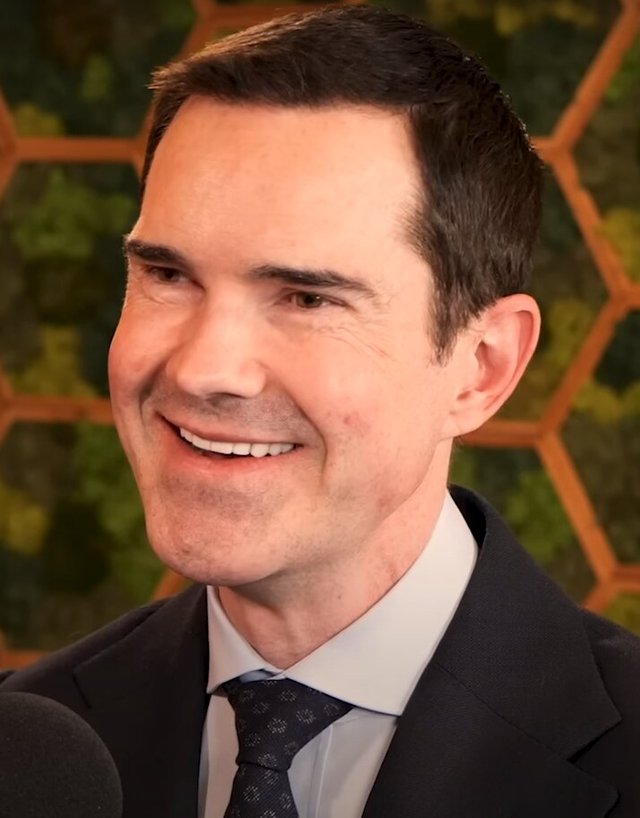 Close-up portrait of a smiling man in a dark suit and tie speaking into a microphone